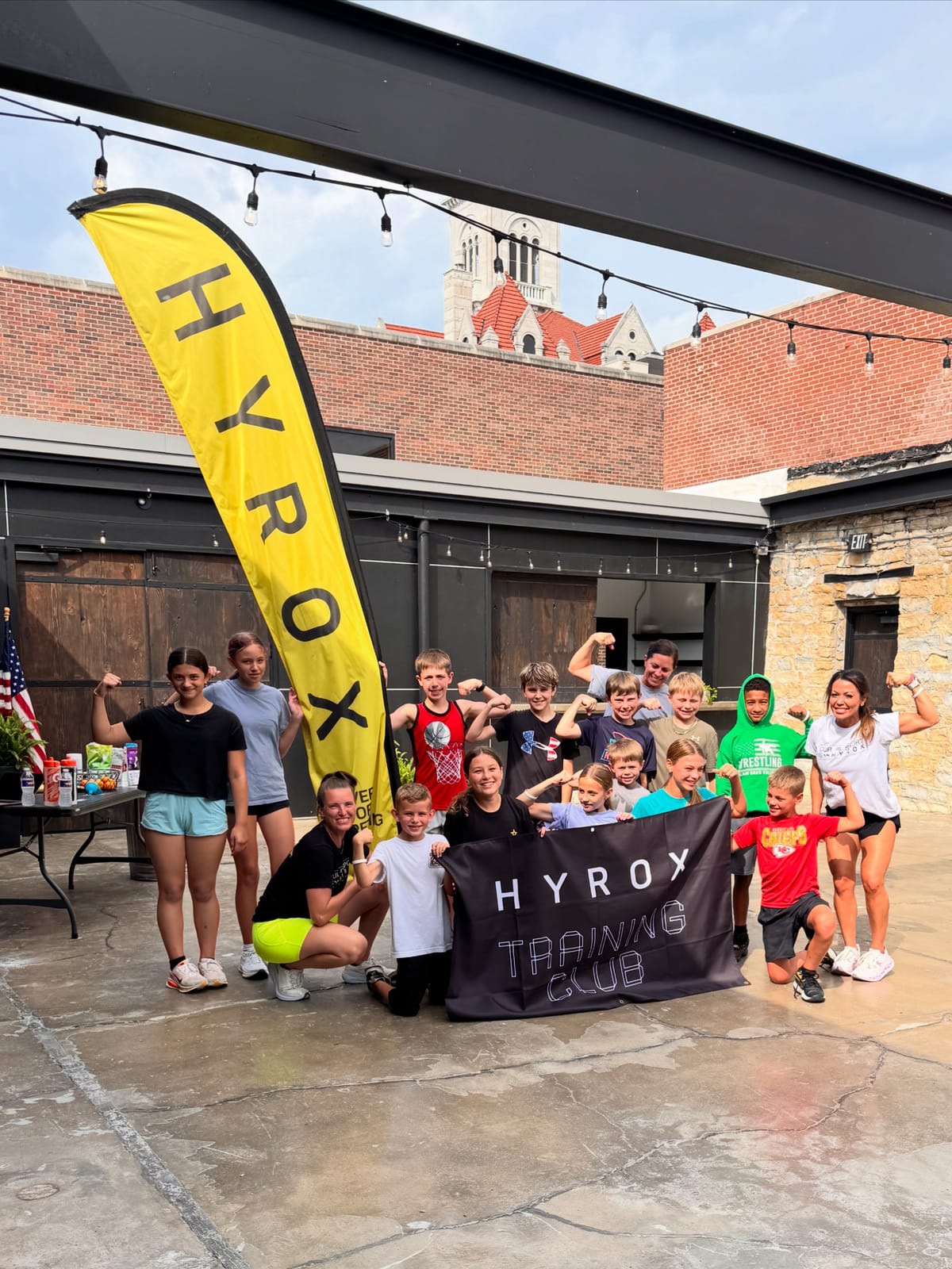 SOULRNR youth training club — kids flexing with the HYROX Training Club banner in the courtyard
