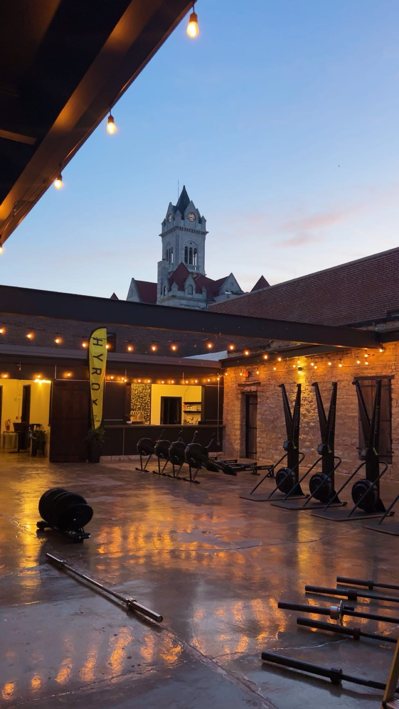 The SOULRNR courtyard at dusk — string lights, HYROX flag, and race equipment under the courthouse tower