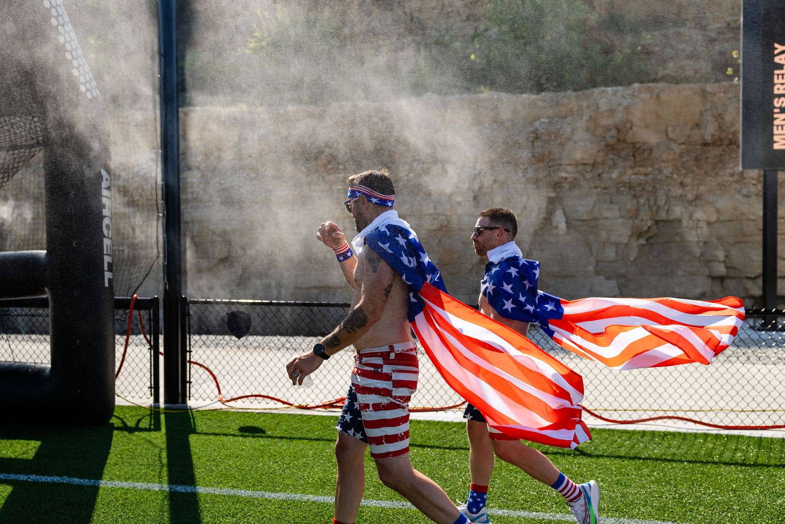 Athletes in American flag capes running through mist